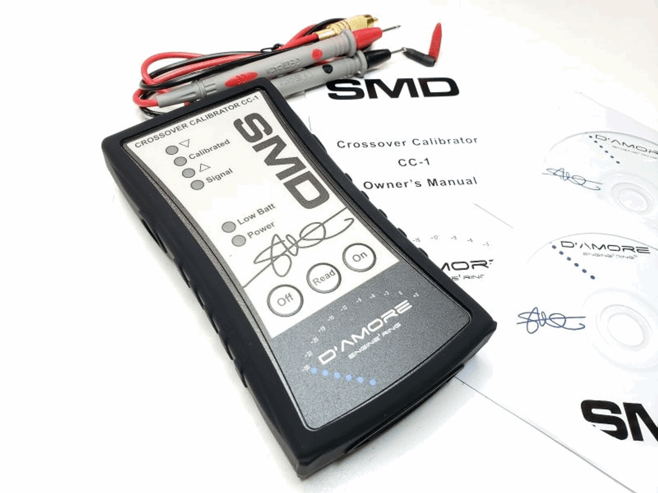 The SMD Crossover Calibrator CC-1 by Steve Meade Designs, perfect for gain matching of amplifiers, comes equipped with an LCD display and buttons for power, open, read, and off functions. It includes testing probes, a user manual, and CDs—all elegantly displayed on a white surface.