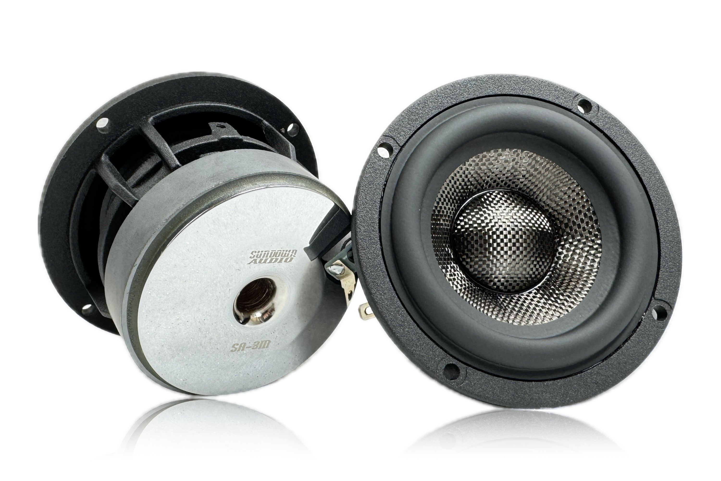 Two Sundown Audio SA-Series SA-3M 4ohm 3 speakers, in black and silver, are on a reflective surface. One stands upright showing its grid-patterned carbon fiber cone, while the other reveals the metal base. Partially visible brand text suggests exceptional clarity.