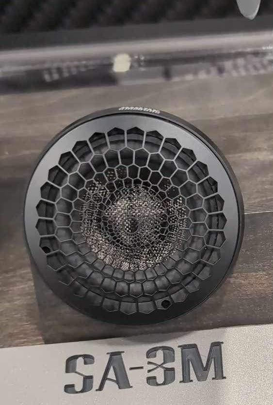 Close-up of a round Sundown Audio SA-Series SA-3M 3" speaker featuring a metal honeycomb grille design with detailed mesh behind it. The model label, "SA-3M," is visible at the bottom. With its full-range capabilities, it captures every detail, while the blurred background highlights the speaker unit.