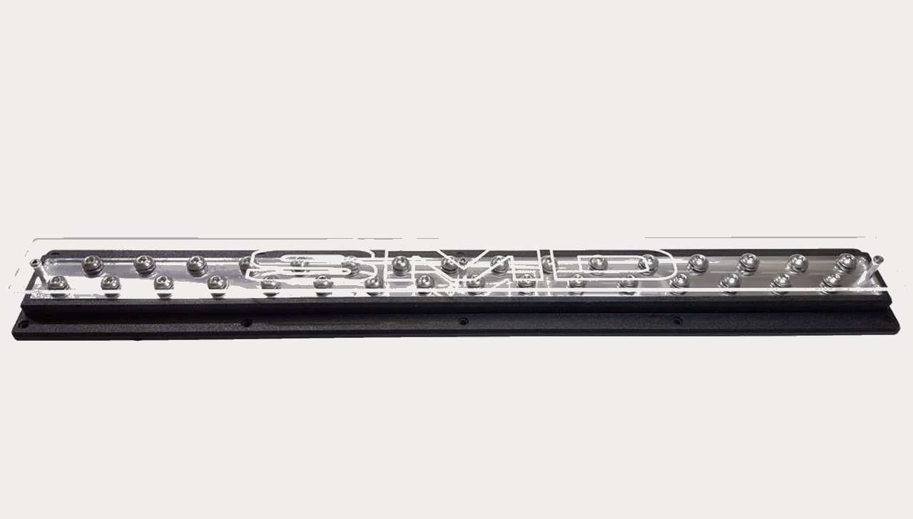 The SMD 25" Power - Ground distribution bar by Steve Meade Designs features a modern, rectangular LED light bar with clear cover and distinctive metal lettering. With evenly spaced bulbs nestled in a metallic frame, it is mounted on a sleek black base set against a plain white background, echoing precision found in car audio systems.